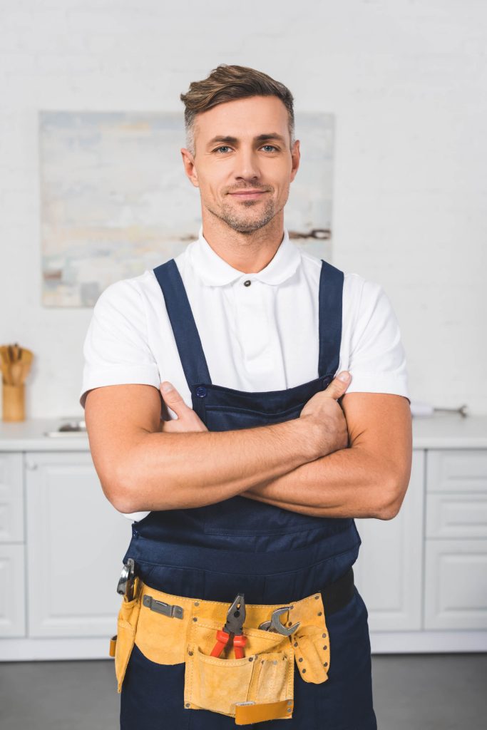 A man wearing overalls stands in a kitchen, surrounded by cooking utensils and appliances, ready to prepare a meal.