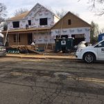 A house under construction with scaffolding, featuring a parked car in front on a clear day.